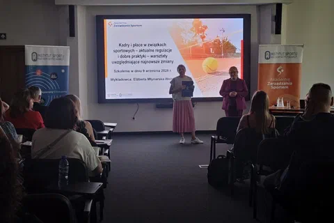 Dwie kobiety stojące przed ekranem z prezentacją wprowadzającą do szkolenia o kadrach i płacach.