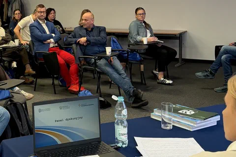 Troje uczestników rozmawiających w kręgu za stołem z laptopem i materiałami szkoleniowymi.
