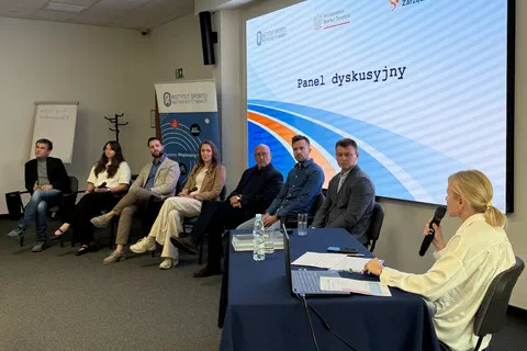 Moderatorka zadająca pytanie uczestnikom panelu dyskusyjnego na tle ekranu projekcyjnego.