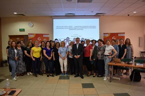 Grupowe zdjęcie uczestników i prowadzących szkolenie Akademii Zarządzania Sportem w sali wykładowej przed ekranem z prezentacją o przepisach podatkowych (VAT, CIT, PIT i ZUS w 2022 r.) w działalności sportowej