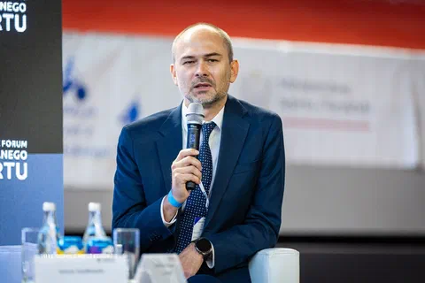 Zbliżenie na uczestnika debaty wypowiadającego się do mikrofonu przy stoliku z wodą.