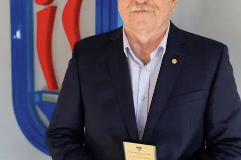 Wyróżniony w marynarce prezentujący złoty medal w otwartym etui na tle znaku Instytutu Sportu.