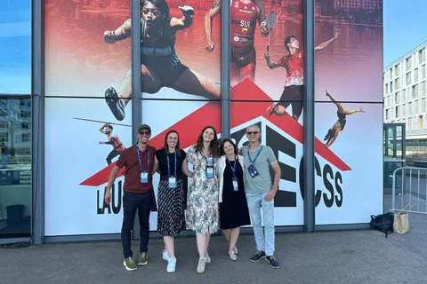 Pięcioro uczestników kongresu pozujących przed wielkoformatowym banerem ECSS Lausanne 2026 ze zdjęciami sportowców.