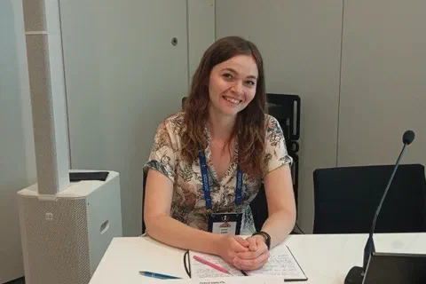 Uczestniczka siedząca za stołem prezydialnym z mikrofonem i tabliczką imienną przed sesją naukową.
