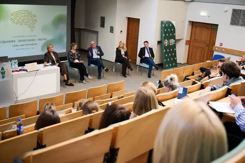 Pięcioro uczestników panelu dyskusyjnego siedzących na krzesłach przed widownią w auli wykładowej.