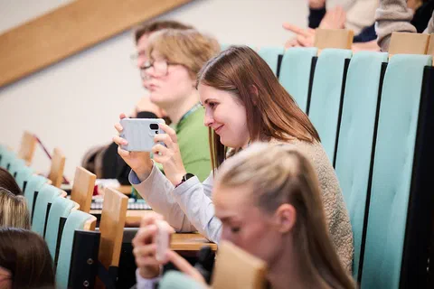 Uczestniczka na widowni auli fotografująca telefonem prezentację wyświetlaną podczas sesji.