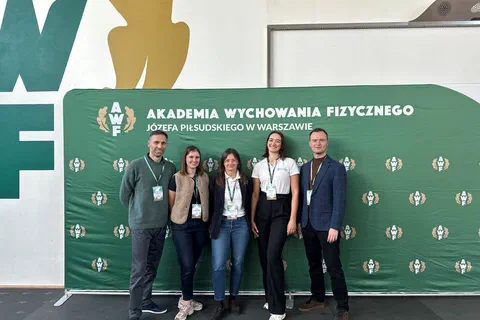 Pięcioro prelegentów pozujących wspólnie na tle zielonej ścianki Akademii Wychowania Fizycznego w Warszawie.