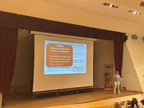Prelegentka przy mównicy podczas prezentacji o zrównoważonym rozwoju i kulturze w sporcie wyczynowym na konferencji ENYSSP 2025