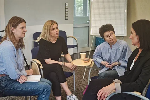 Cztery kobiety dyskutujące w podgrupie obok białej tablicy flipchart.