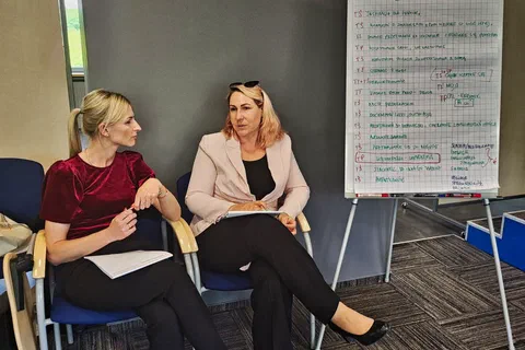 Dwie uczestniczki rozmawiające obok flipchartu zapisanego wnioskami z dyskusji o przywództwie.