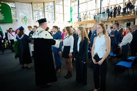 Rektor w todze i gronostajach dokonujący immatrykulacji studentów pierwszego roku za pomocą berła rektorskiego.