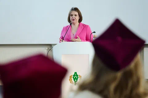 Kobieta w różowym żakiecie zabierająca głos z mównicy z godłem AWF Warszawa.
