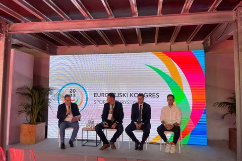 Czterej uczestnicy debaty siedzący na scenie przed ekranem z logo Europejskiego Kongresu Sportu i Turystyki.