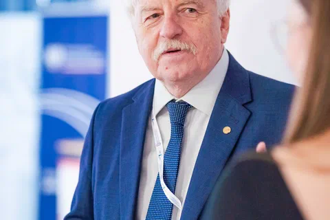 Mężczyzna w granatowym garniturze podczas wystąpienia przed uczestnikami konferencji.
