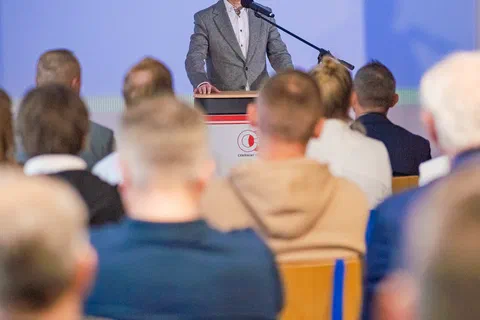 Wystąpienie przy mównicy na tle niebieskiej ścianki Ministerstwa Sportu i Turystyki.