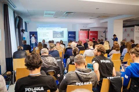 Sala konferencyjna wypełniona trenerami i uczestnikami słuchającymi prezentacji.