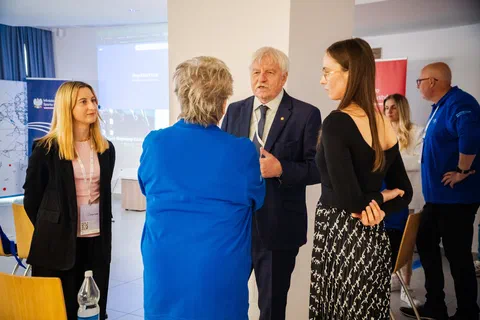 Rozmowa pięciorga uczestników konferencji w kuluarach sali wykładowej.