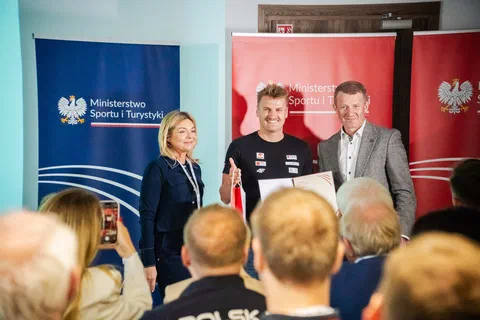 Wręczenie wyróżnienia trenerowi na tle banerów Ministerstwa Sportu i Turystyki.