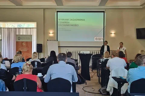 Dwaj prelegenci stojący przy ekranie z prezentacją o wybranych zagadnieniach z zakresu rachunkowości.