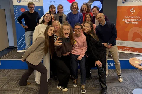 Uczestniczki i prowadzący robiący wspólne selfie w sali szkoleniowej.