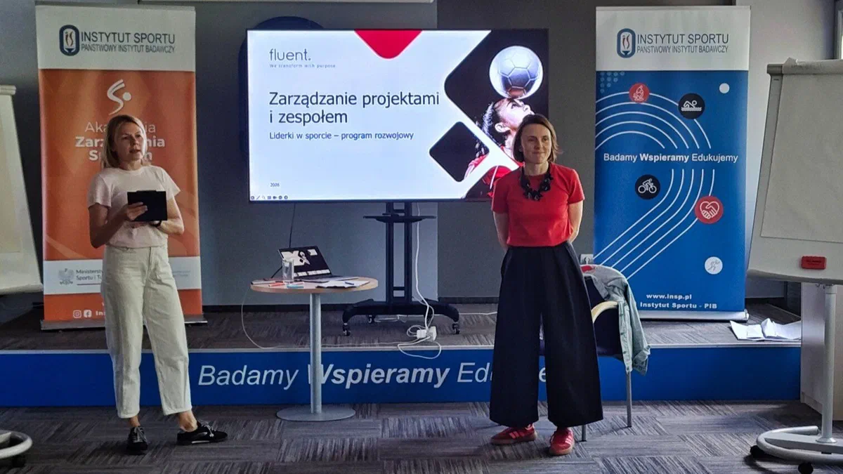 Dwie prowadzące w sali szkoleniowej Instytutu Sportu – PIB przed ekranem z prezentacją „Zarządzanie projektami i zespołem” w programie „Liderki w sporcie”.