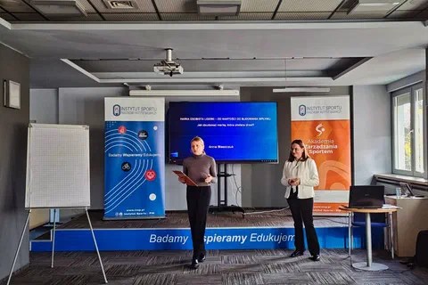 Dwie prowadzące stojące przed ekranem z prezentacją i roll-upami podczas otwarcia szkolenia w sali konferencyjnej
