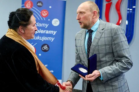 Wręczenie medalu Instytutu Sportu kobiecie w czarnej marynarce i szalu na tle roll-upu z hasłem Badamy Wspieramy Edukujemy