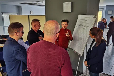 Pięcioosobowy zespół stojący wokół flipchartu i zapisujący wnioski podczas pracy w grupach