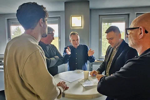 Czterech mężczyzn rozmawiających i robiących notatki przy okrągłym stoliku koktajlowym