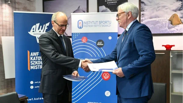 Uścisk dłoni przedstawicieli Instytutu Sportu – PIB i AWF Katowice po podpisaniu porozumienia o współpracy na tle roll-upów obu instytucji.