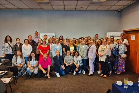 Wspólne zdjęcie dużej grupy uczestników szkolenia ustawionych w dwóch rzędach w przestronnej sali