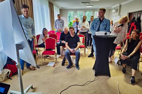Dwaj uczestnicy omawiający notatki na flipcharcie przed grupą siedzącą w półkolu