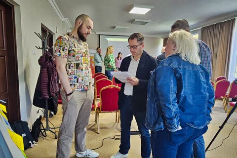 Trzy osoby dyskutujące nad kartką z notatkami podczas pracy warsztatowej w sali