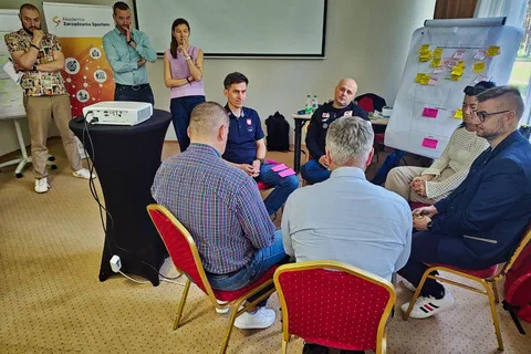 Czterech mężczyzn naradzających się w kręgu na krzesłach obok flipchartu z żółtymi karteczkami