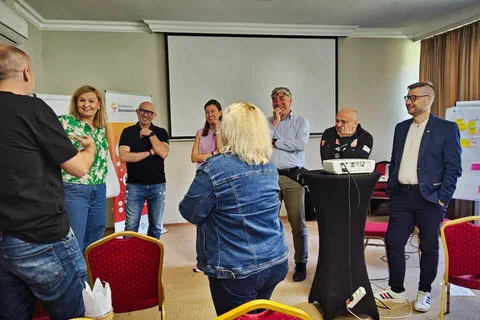 Sześcioosobowa grupa rozmawiająca na stojąco wokół stolika z projektorem podczas ćwiczenia