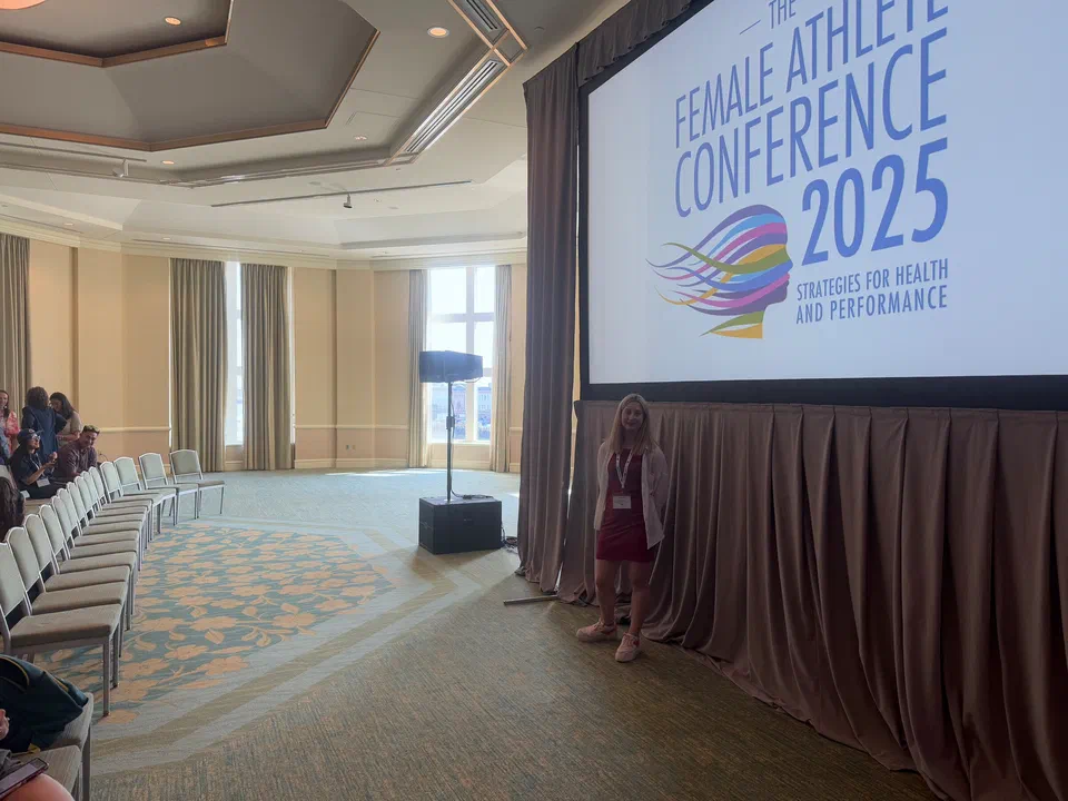 Prelegentka na scenie pod ekranem z napisem „The Female Athlete Conference 2025 – Strategies for Health and Performance”