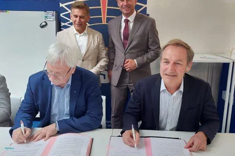 Dwaj dyrektorzy podpisujący przy stole porozumienie o współpracy w obecności dwóch stojących za nimi mężczyzn
