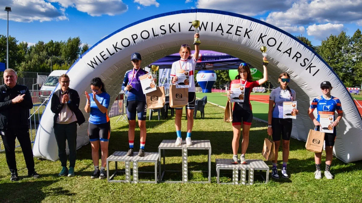 Młodzi kolarze na podium pod dmuchaną bramą Wielkopolskiego Związku Kolarskiego podczas zawodów w Śremie.