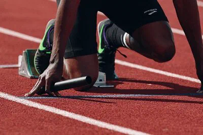 Sprinter z pałeczką sztafetową w blokach startowych na bieżni lekkoatletycznej